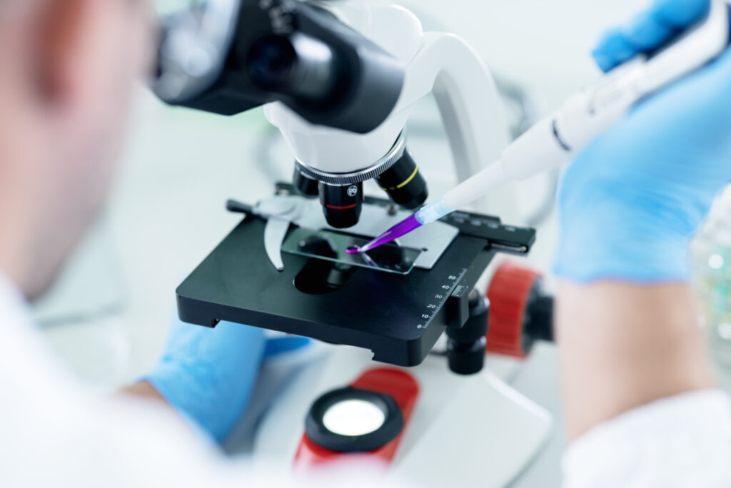 Stock image of male researcher analyzing scientific and chemical samples using a laboratory microscope.