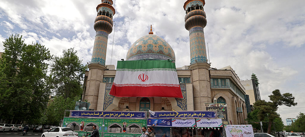 Motorists ride past the Imam Sadiq (AS) mosque with a giant Iranian flag installed on its front at the Palestine Square in Tehran on April 19, 2026. The strategic Strait of Hormuz was again closed on April 19