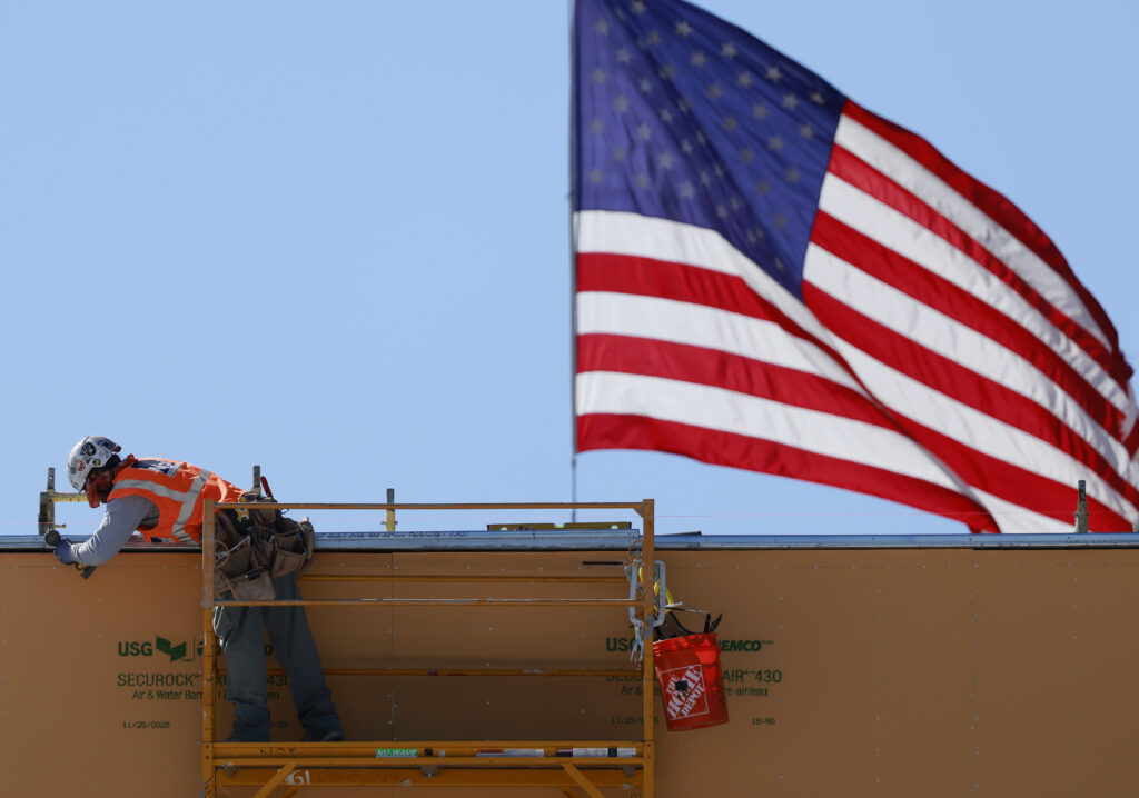 An American flag flies near a construction worker during construction of a new building on March 6, 2026