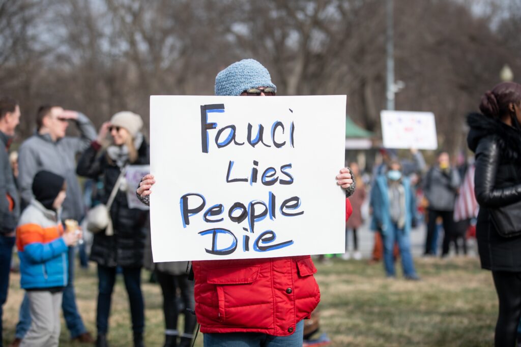 A protester in a red jacket holds a handmade "Fauci Lies People Die" sign at a Washington, D.C., vaccine mandate rally.