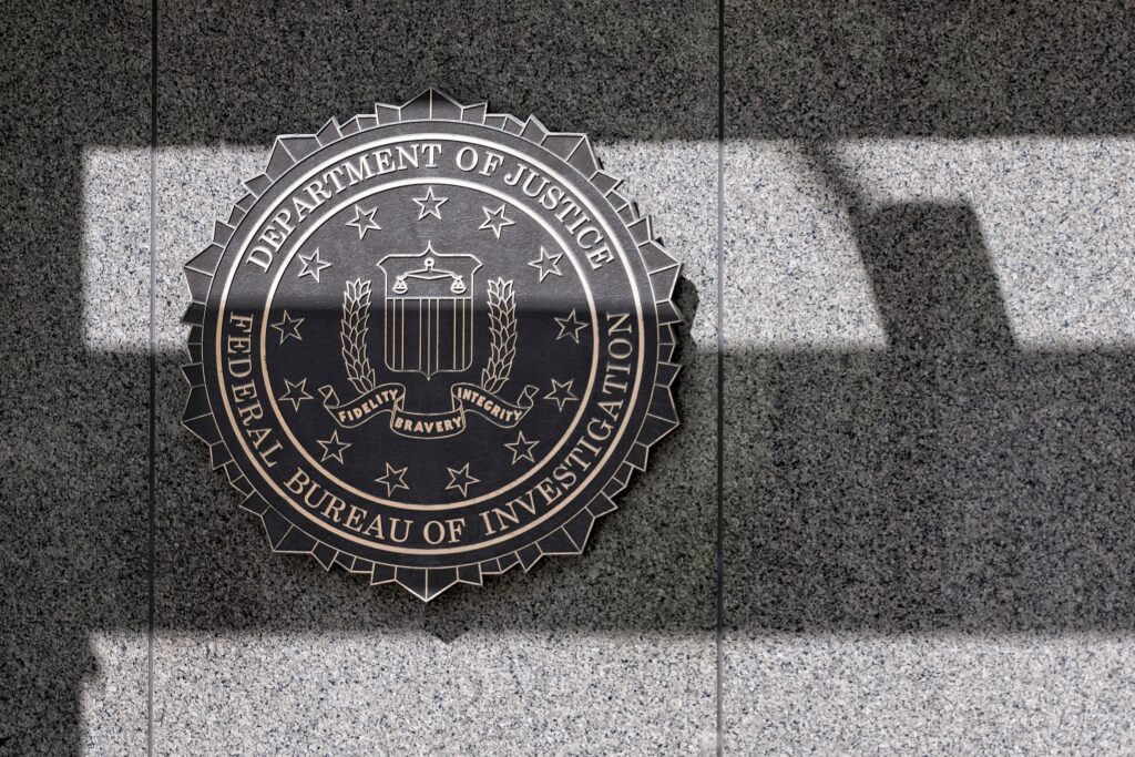 The FBI seal on the granite facade of the J. Edgar Hoover Building in Washington, D.C., crossed by bands of light and shadow.