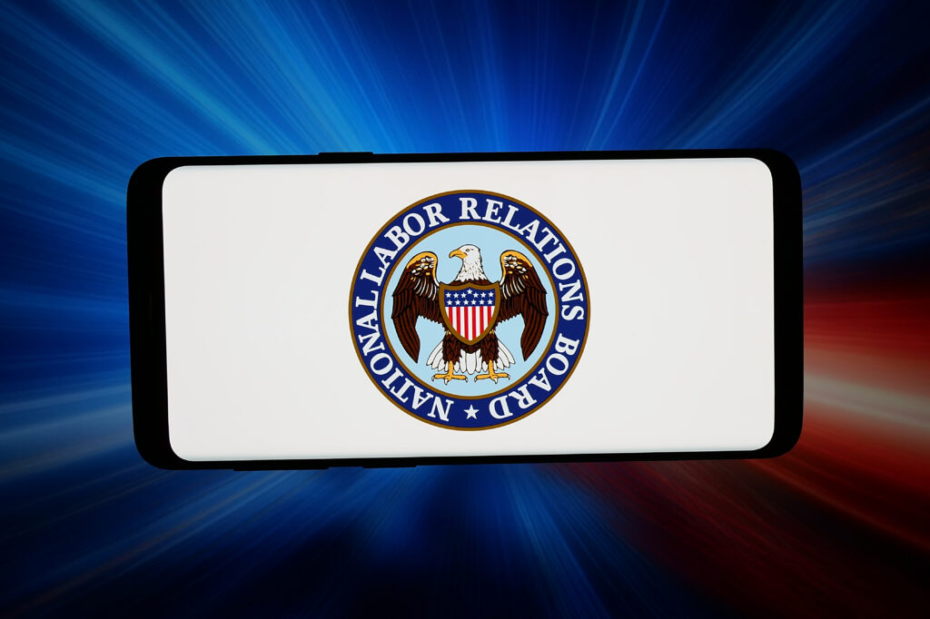 In this photo illustration, the logo of agency National Labor Relations Board (NLRB) is seen displayed on a smartphone in front of an abstract background on a computer screen.